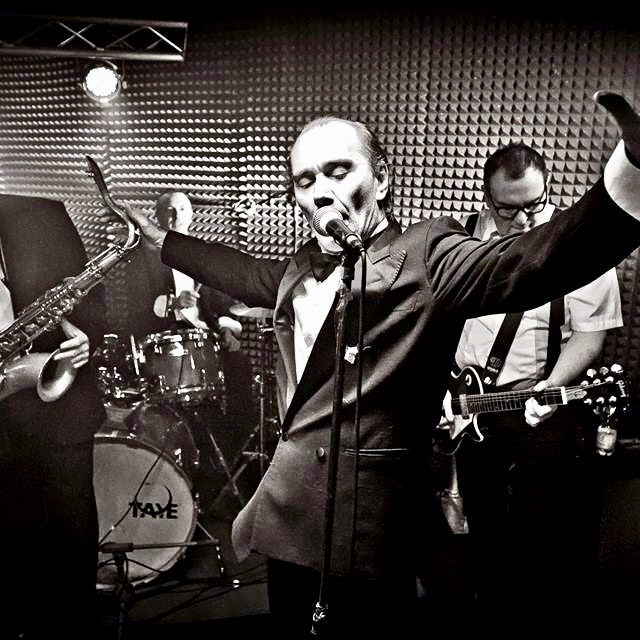 Il cantante a braccia aperte, con il sax e la batteria alle spalle